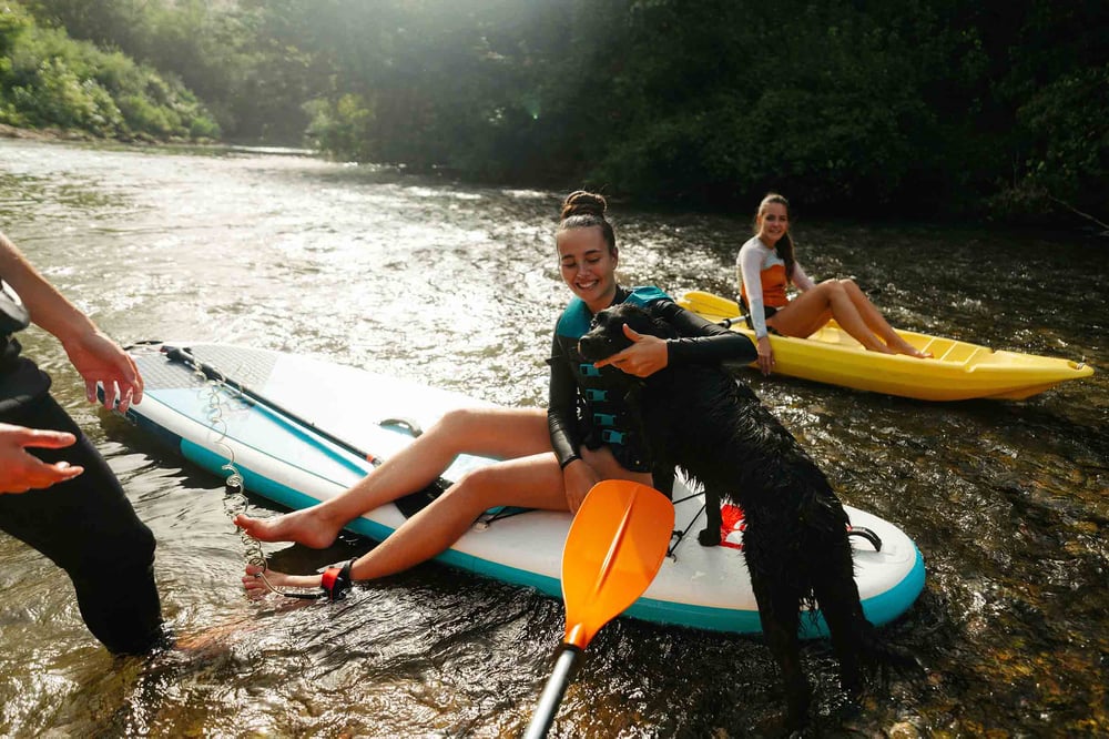 People paddle boarding on a river with a dog