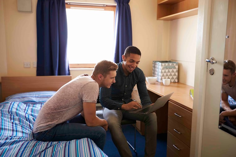 Two friends sitting on a bed in a dorm room