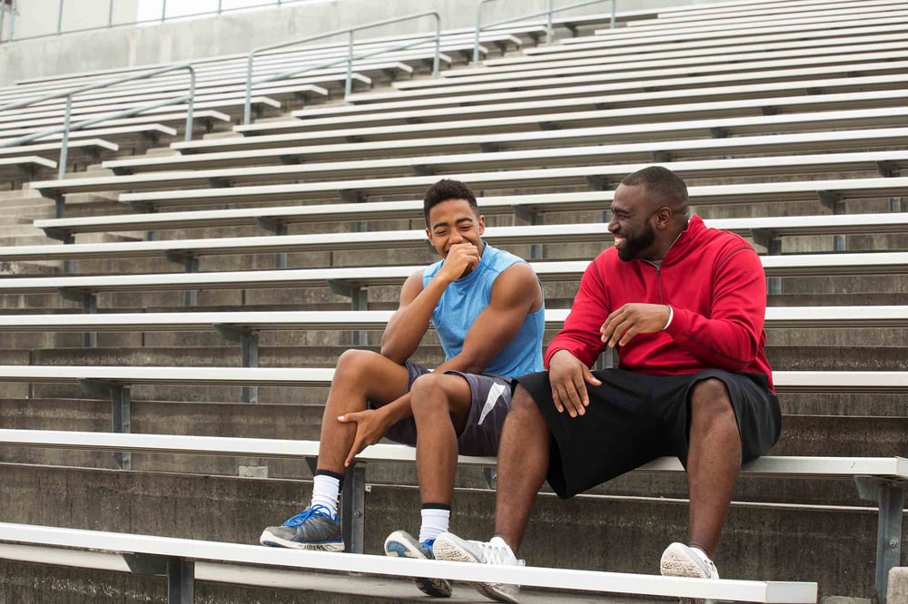 Two people laughing and sitting in bleachers