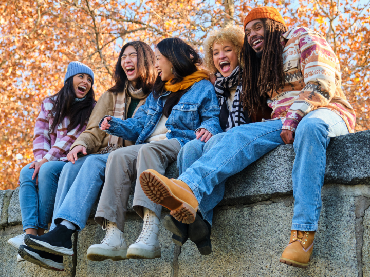 Group of friends sitting on a ledge outdoors, smiling and laughing together.