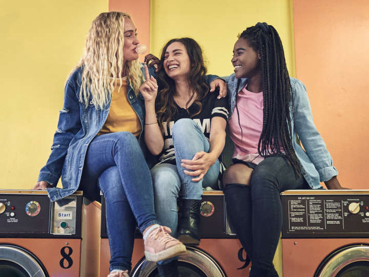 group of 3 friends sitting on top of washing machines at the laundromat