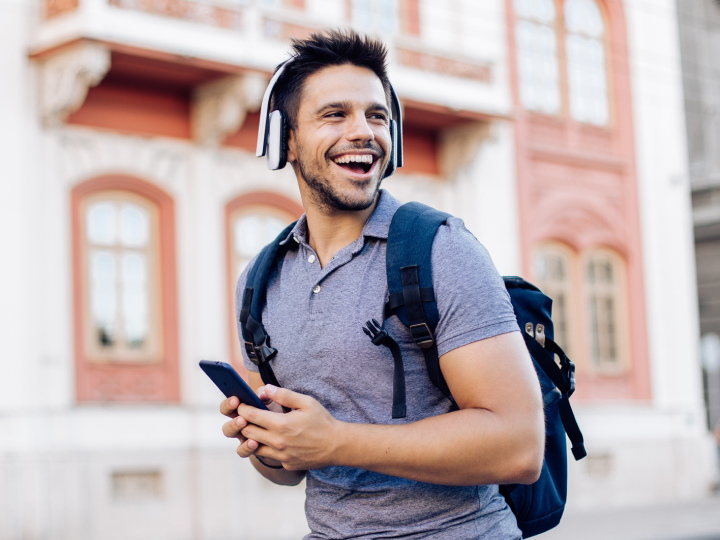 Student walking with headphones on and holding a smartphone in his hands